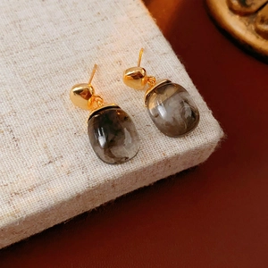 Detail view of oval resin earrings with gold plating on a textured display pad