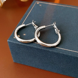 Close-up of polished silver geometric hoop earrings on a blue textured jewelry box