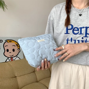Close-up of light blue quilted makeup bag with cloud texture held by a person in a room