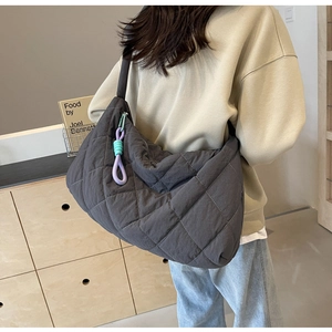 Rear view of a model wearing a grey quilted padded shoulder bag with diamond stitching