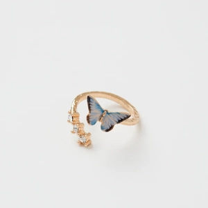 Détail d'une bague dorée ajustable avec papillon dégradé bleu et gemmes scintillantes