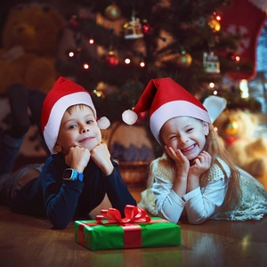 Kids wearing plush red Christmas hats in a warm festive setting with a Christmas tree