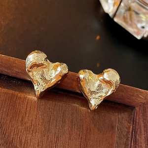 Détail macro de boucles d'oreilles cœur dorées avec texture de métal liquide froissé
