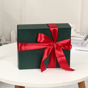 Elegant dark green Christmas gift box with large red ribbon bow on a white table display