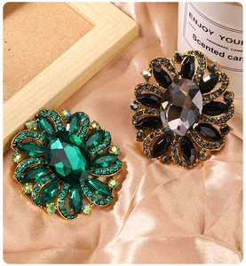 Close-up of vintage floral brooches with green and grey crystals on silk fabric background
