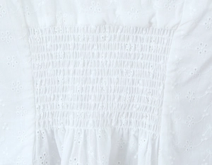 Dettaglio di camicia bianca con ricamo floreale, pizzo sangallo e design arricciato