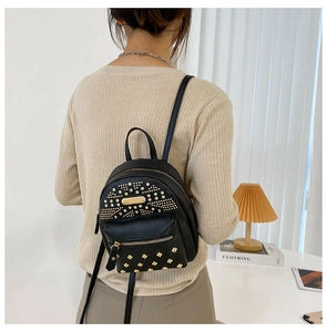 Detail of a black mini backpack with golden rivets and earphone hole on a model