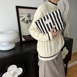 Detail of a minimalist black and white striped knit cosmetic bag with an embroidered label
