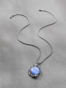 Vue détaillée de la chaîne torsadée en argent avec pendentif rond en œil de chat bleu