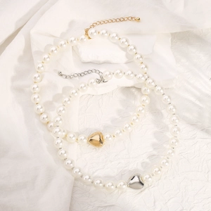 Detailed close-up of pearl necklaces with gold and silver heart pendants on white fabric