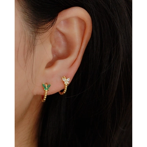 Close-up of vintage butterfly hoop earrings with green and white gemstones on a model