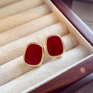Macro view of red enamel stud earrings with gold metal frame in a beige velvet jewelry box