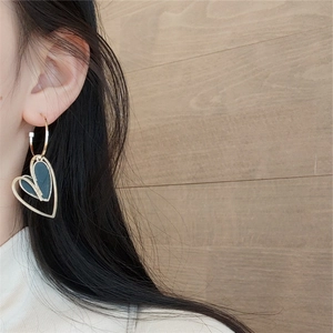 Close-up of asymmetric heart tassel earrings in gold and black on a model's ear