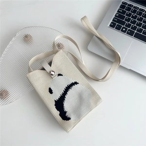 Mini knitted white panda phone crossbody bag on a modern desk with laptop and decor