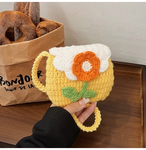 Macro view of hand-knitted yellow bag with 3D orange flower and white cloud flap