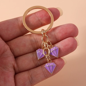 Detail view of purple diamond-shaped keychain pendant held by hand on orange backdrop