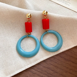 Detail of geometric resin pendant earrings featuring red and blue contrast design with gold