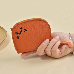 Cute orange cat-shaped wallet in litchi leather held by hand on beige background