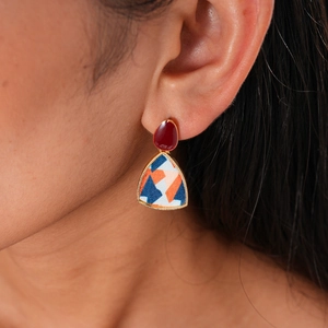 Detailed view of resin geometric earrings with gold trim and red droplet stud on model