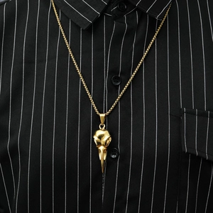 Detailed view of a gold bird skull pendant on a necklace worn over a striped shirt