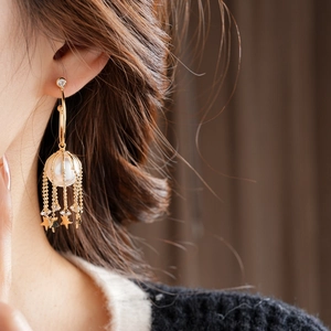 Détail macro de boucles d'oreilles dorées à pampilles étoiles avec perle et cristaux