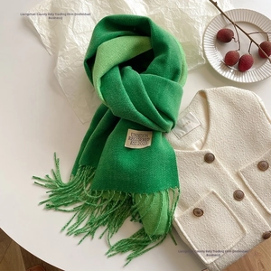 Detail view of grass green faux cashmere scarf with fringe and white woven label