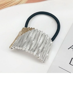 Detail of the arch-shaped metal hair tie with striped texture and gold-silver finish
