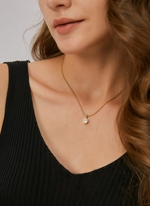 Close-up of minimalist gold necklace with a single round white zircon on a model's neck