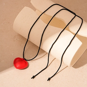 Close-up of a red 3D heart pendant on a black braided cord against a beige texture