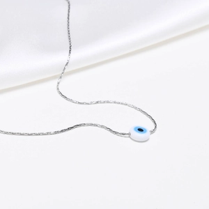 Detail of silver evil eye pendant on a fine chain over elegant white silk fabric