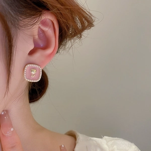 Detail of pink enamel square earring with golden tulip relief and faux pearls on ear