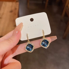 Macro detail of gold halo earrings featuring deep blue square stones and crystal accents