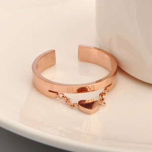 Rose gold open ring with Roman numerals and heart charm displayed on a white plate