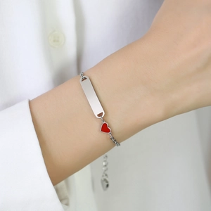 Gros plan d'un bracelet en acier inoxydable avec plaque à graver et breloque coeur rouge