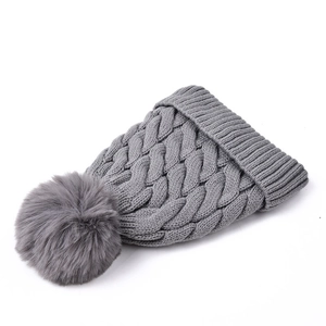 Detail of grey cable knit beanie showing thick weave texture and fluffy faux fur pom-pom