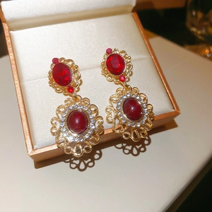 Close-up of vintage gold filigree earrings with red crystals in a gold gift box