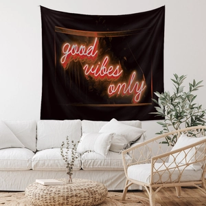 Detail of black tapestry with red neon Good Vibes Only text above a white sofa
