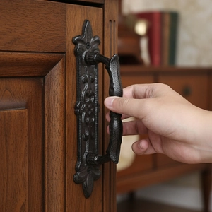 European vintage cast iron door handle with ornate floral relief on dark wood cabinet