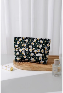 Detailaufnahme der schwarzen Make-up-Tasche mit Gänseblümchen-Stickerei auf Holztablett