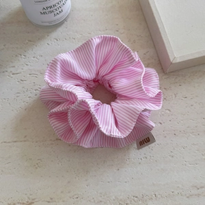 Macro detail of high-elasticity pink striped scrunchie with m label on stone surface