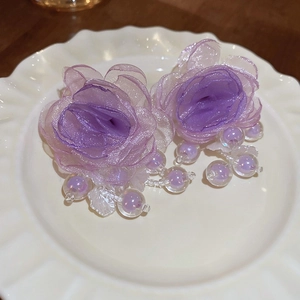 Detailed view of purple mesh flower earrings with iridescent beads on a white tray