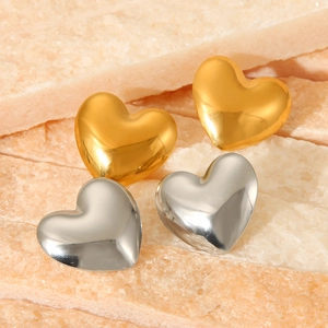 Macro shot of gold and silver heart-shaped stud earrings on a textured stone surface