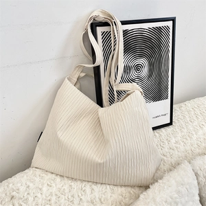 Detail of creamy white pleated canvas bag with adjustable strap on plush white surface