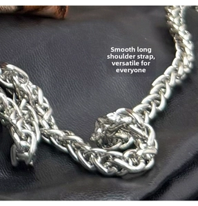 Close-up of a glossy silver metal chain shoulder strap for handbags on black leather