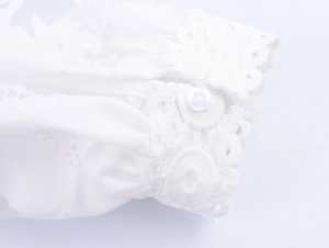 Close-up of white lace cuff with delicate embroidery and round button closure