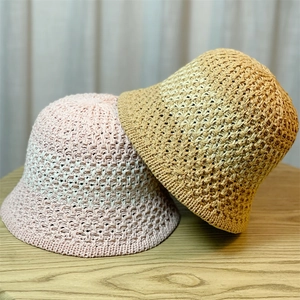Detail of hand-crocheted hollow-out knit bucket hats in pink and khaki on a wooden table