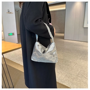 Gros plan du sac à bandoulière à paillettes argentées porté avec un manteau noir chic