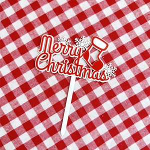 Macro detail of Merry Christmas acrylic cake topper with snowflake and stocking elements