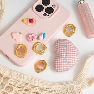 Detailed view of a pink phone case decorated with strawberry, donut, and gold charms