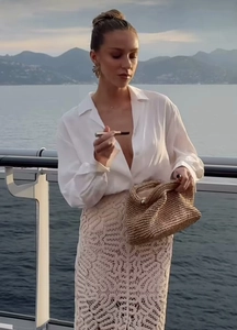Détail de la jupe en dentelle beige et du sac tressé avec vue sur la mer